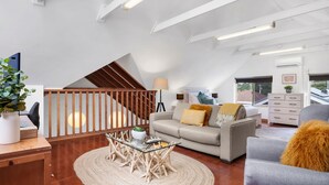 A modern living room with a sofa, a glass coffee table, and a staircase with wooden railings. - Minnamurra Retreat 3 ~ Forget your worries in this spacious and serene space (Minnamurra)