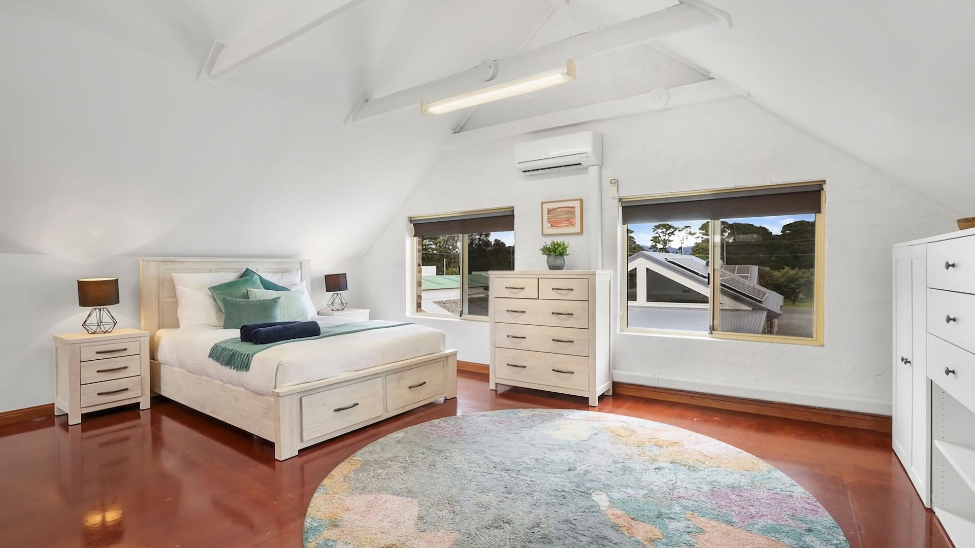A bedroom with a bed, bedside tables, a dresser, a window with a view, and an air conditioning unit.