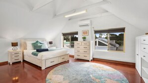 A bedroom with a bed, bedside tables, a dresser, a window with a view, and an air conditioning unit. - Minnamurra Retreat 3 ~ Forget your worries in this spacious and serene space (Minnamurra)
