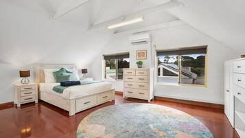 A bedroom with a bed, bedside tables, a dresser, a window with a view, and an air conditioning unit.