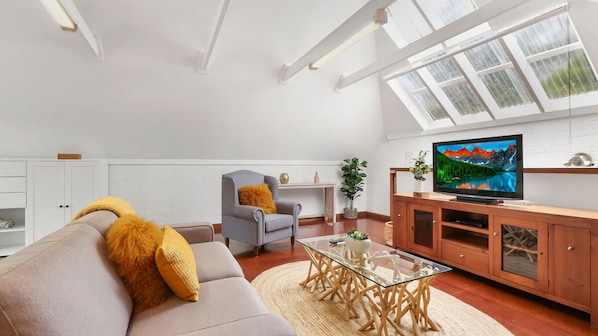 Un salon moderne comprenant un canapé, un fauteuil, une table basse en verre, un meuble de rangement en bois et un téléviseur.