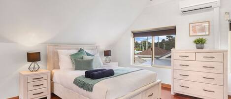 Une chambre à coucher comprenant un lit, des tables de chevet, une commode, une fenêtre avec vue et un appareil de climatisation.