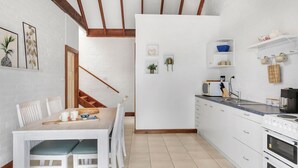 A modern kitchen with white cabinetry, a dining area with a wooden table and chairs, and a staircase leading to another level. - Minnamurra Retreat 3 ~ Forget your worries in this spacious and serene space (Minnamurra)