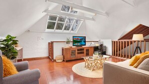 Un salon de style industriel, avec un plafond en pente, un téléviseur, un bureau et un escalier.