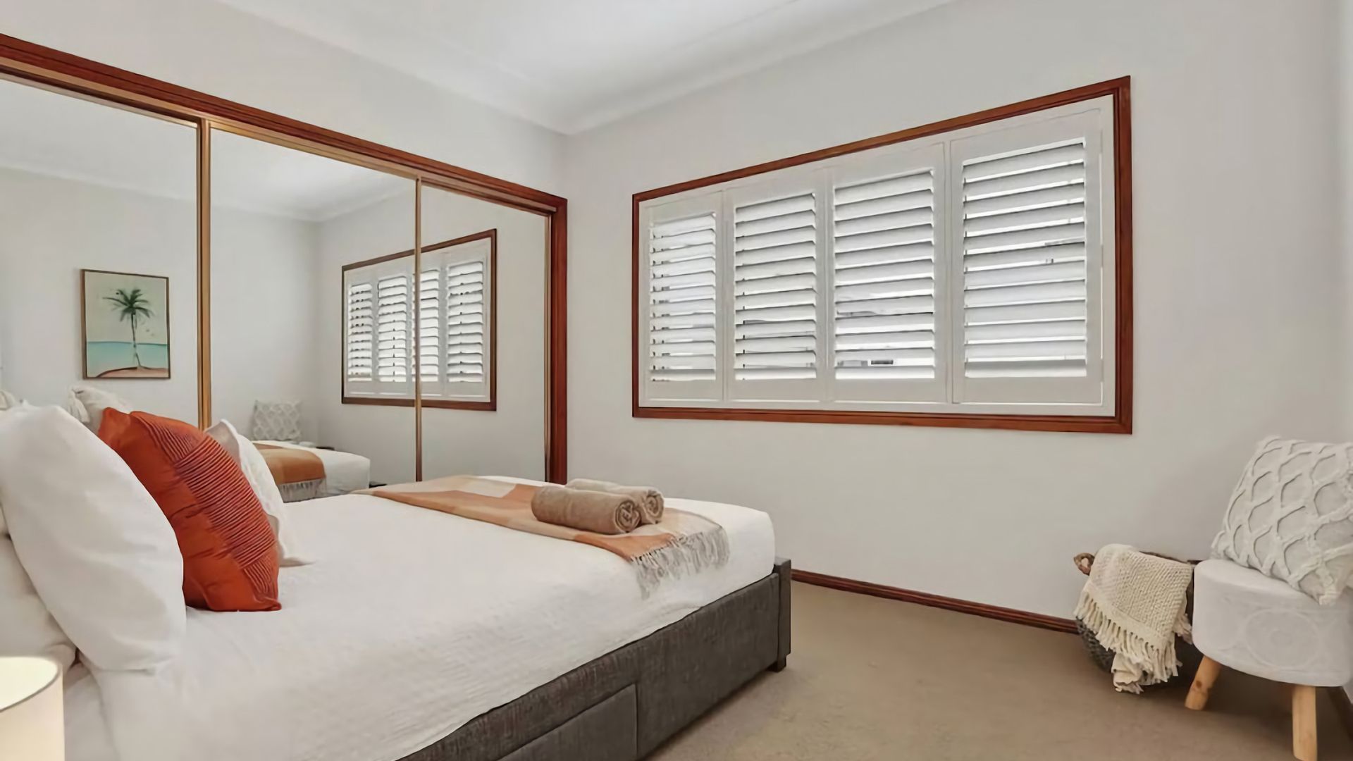 A bedroom with a bed, a chair, a large mirror, and a window with shutters.