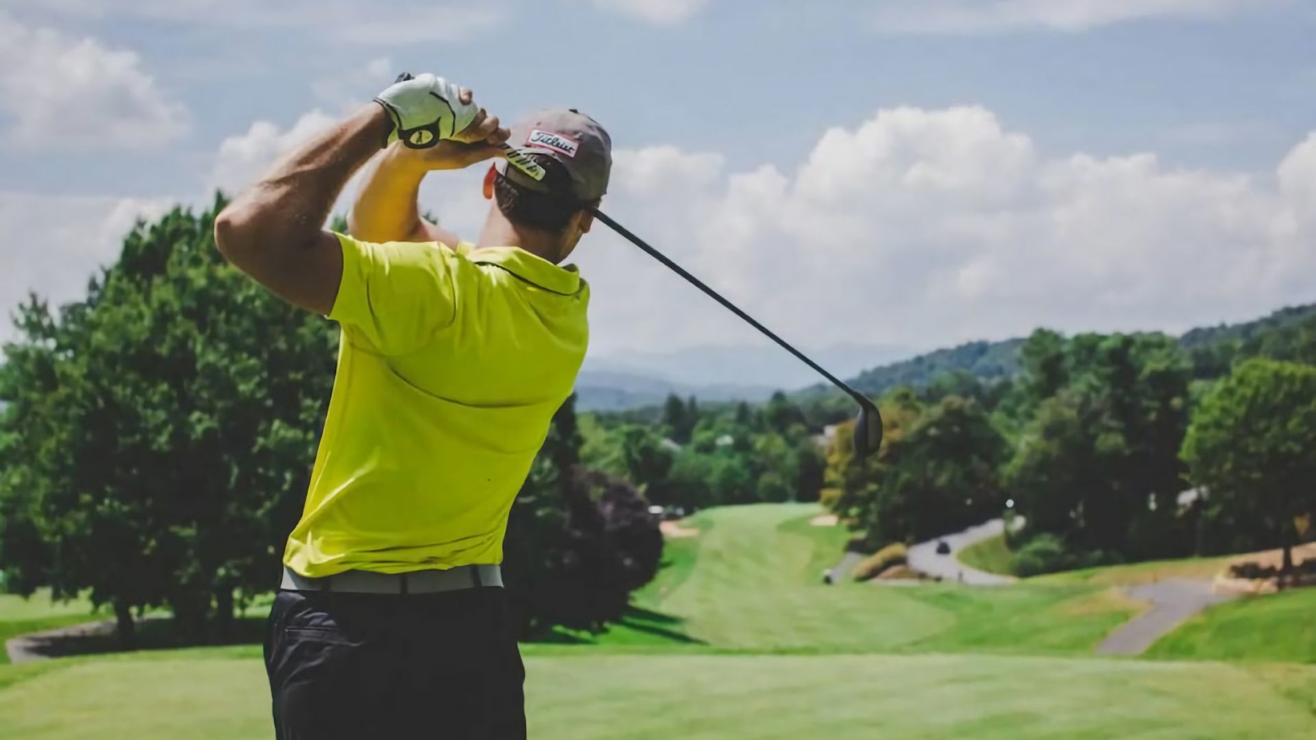 A person in a bright yellow shirt swinging a golf club on a golf course.