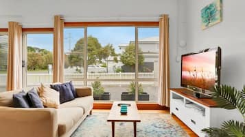 A living room with a sofa, coffee table, TV, and large windows with curtains.