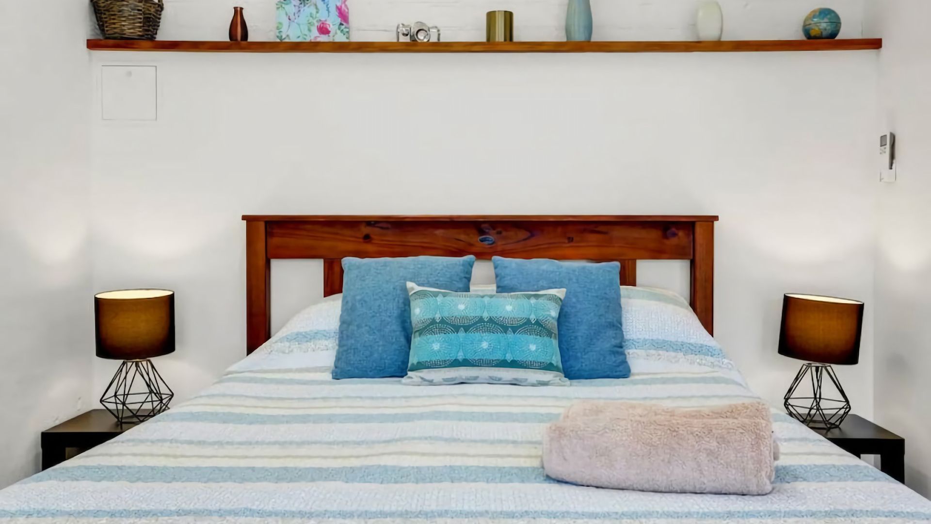 Ein Bett mit Holz-Kopfteil, zwei Nachttischlampen und einer gestreiften Tagesdecke.