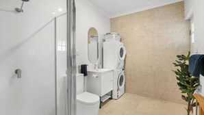 Et lille badeværelse med en glasbrusekabine, toilet og stablede vaskemaskiner.