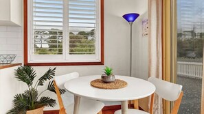 A small round table with a potted plant, white chairs, a window with blinds, and a blue floor lamp. - Minnamurra Retreat ~ Relaxing getaway in a serene and spacious home (Minnamurra)