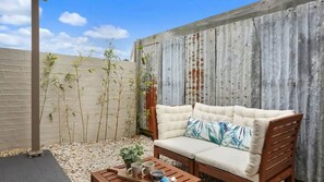 Eine Terrasse mit einer Holzbank, einer gepolsterten Couch und einem Tisch mit Getränken und einer Pflanze.