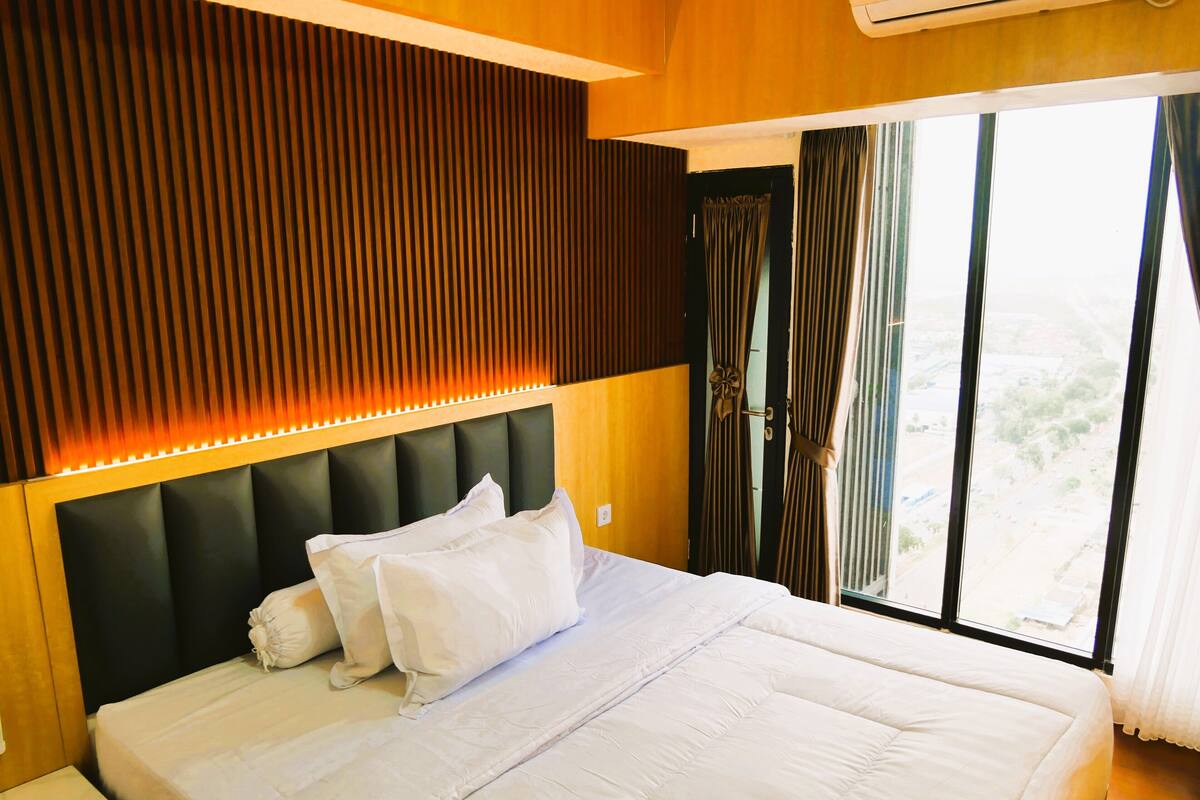 A hotel room with a large bed, a wooden headboard, and a window with curtains.