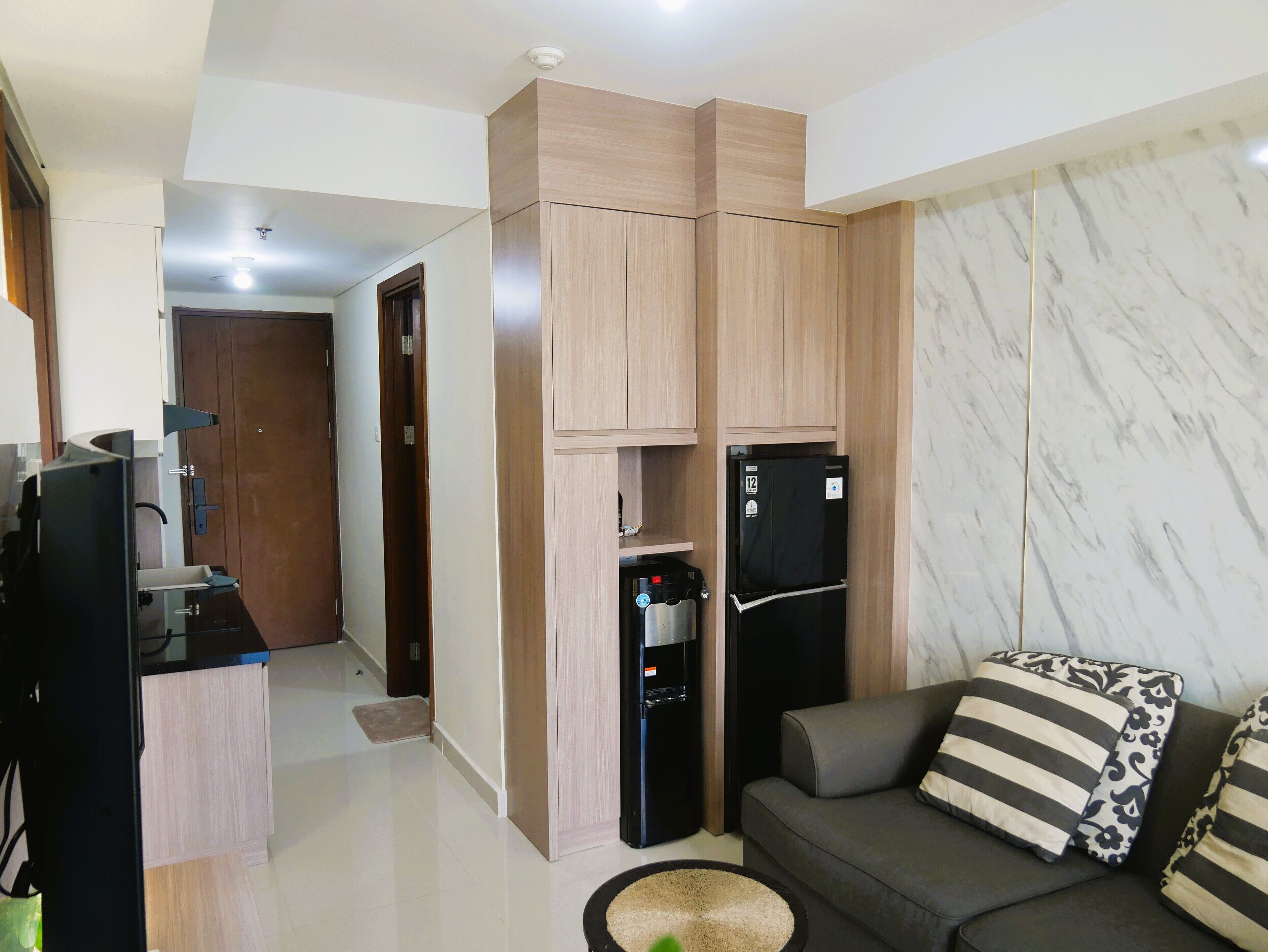 A modern living room with a sofa, a coffee table, and a kitchen area with cabinets and a refrigerator.