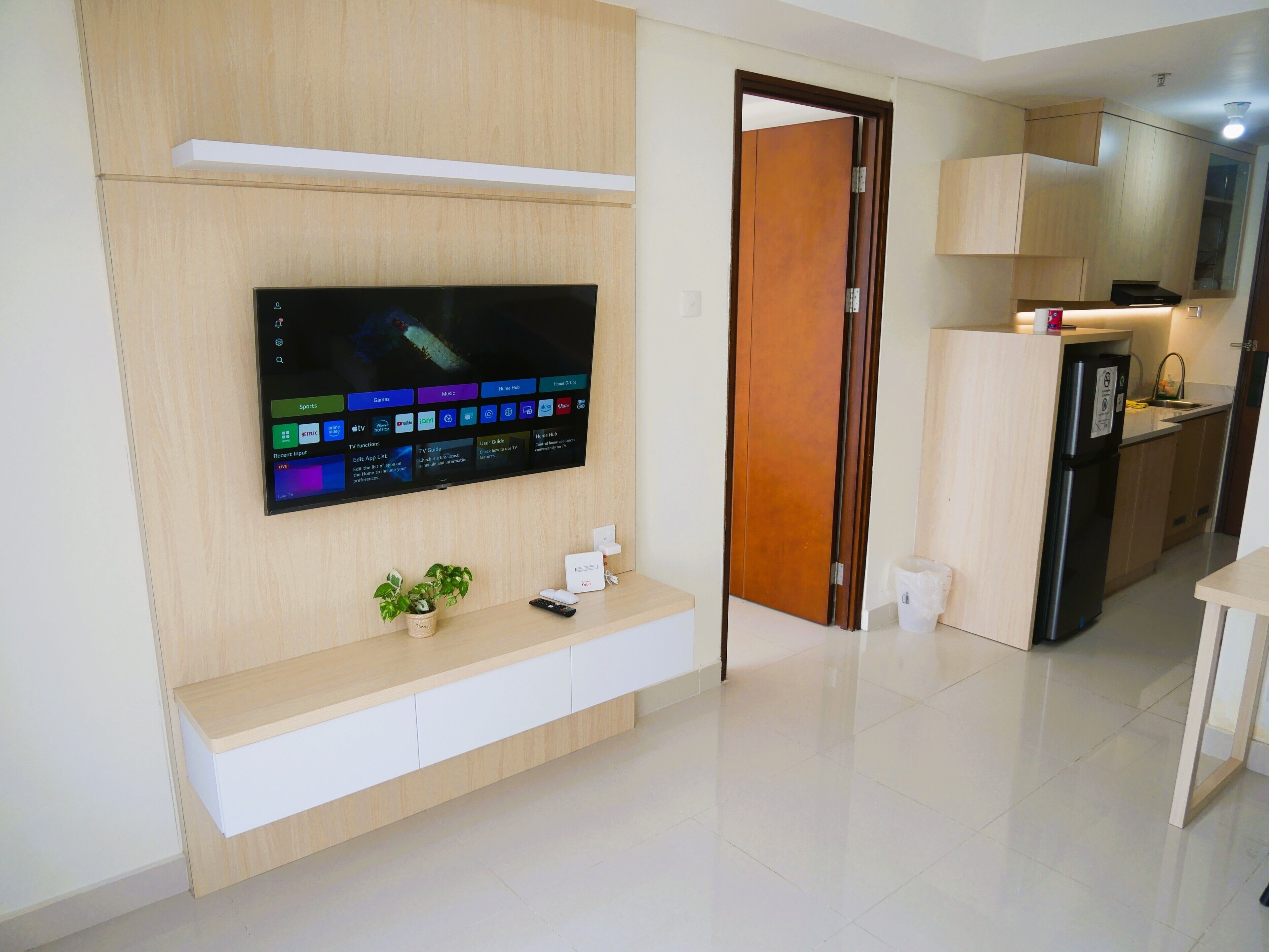 A modern living room with a flat-screen TV mounted on a wooden wall, a small plant, and a remote control on a wooden console.