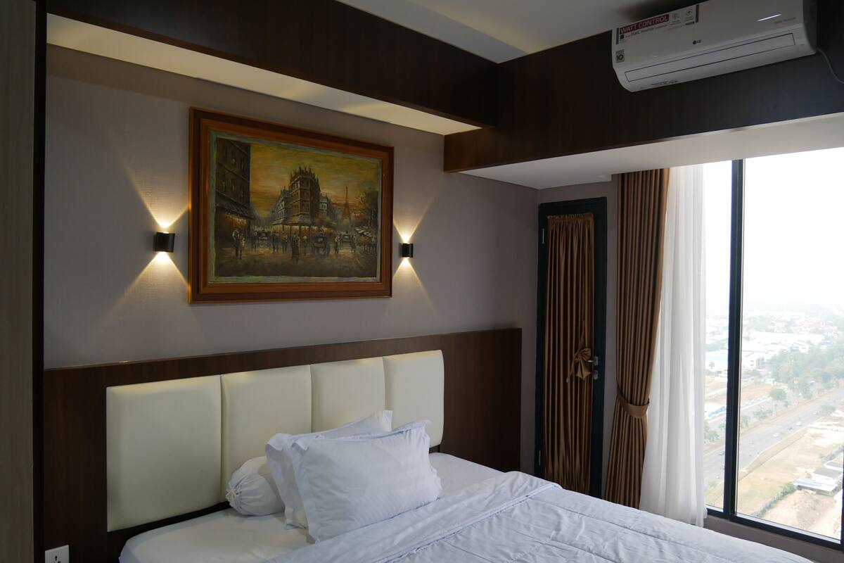 Une chambre d’hôtel avec un lit, un tableau au mur, un appareil de climatisation et une fenêtre donnant sur un beau paysage.