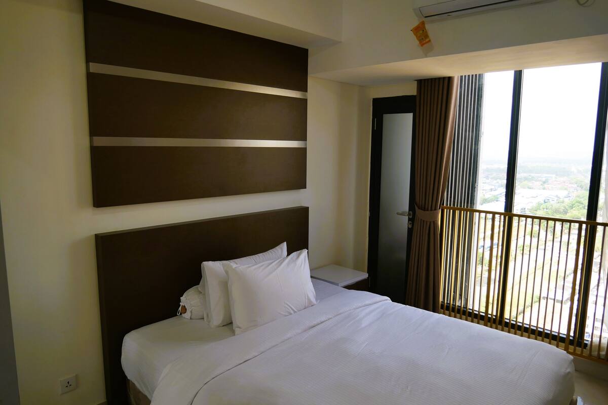 Une chambre d’hôtel avec un grand lit, un climatiseur fixé au mur et une fenêtre donnant sur la ville.