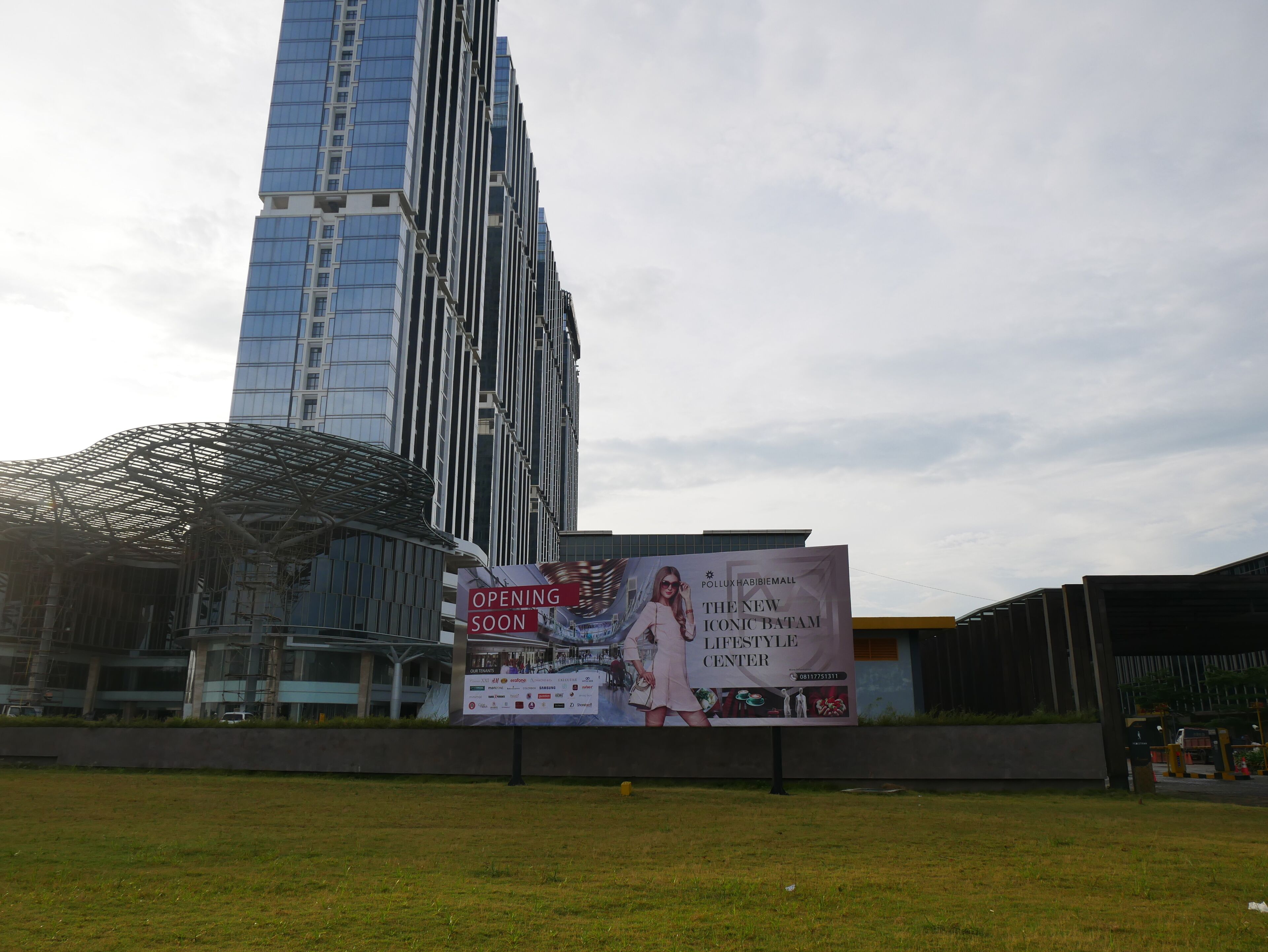 Un gran cartel publicitario de un nuevo centro de estilo de vida, con un edificio moderno al fondo.