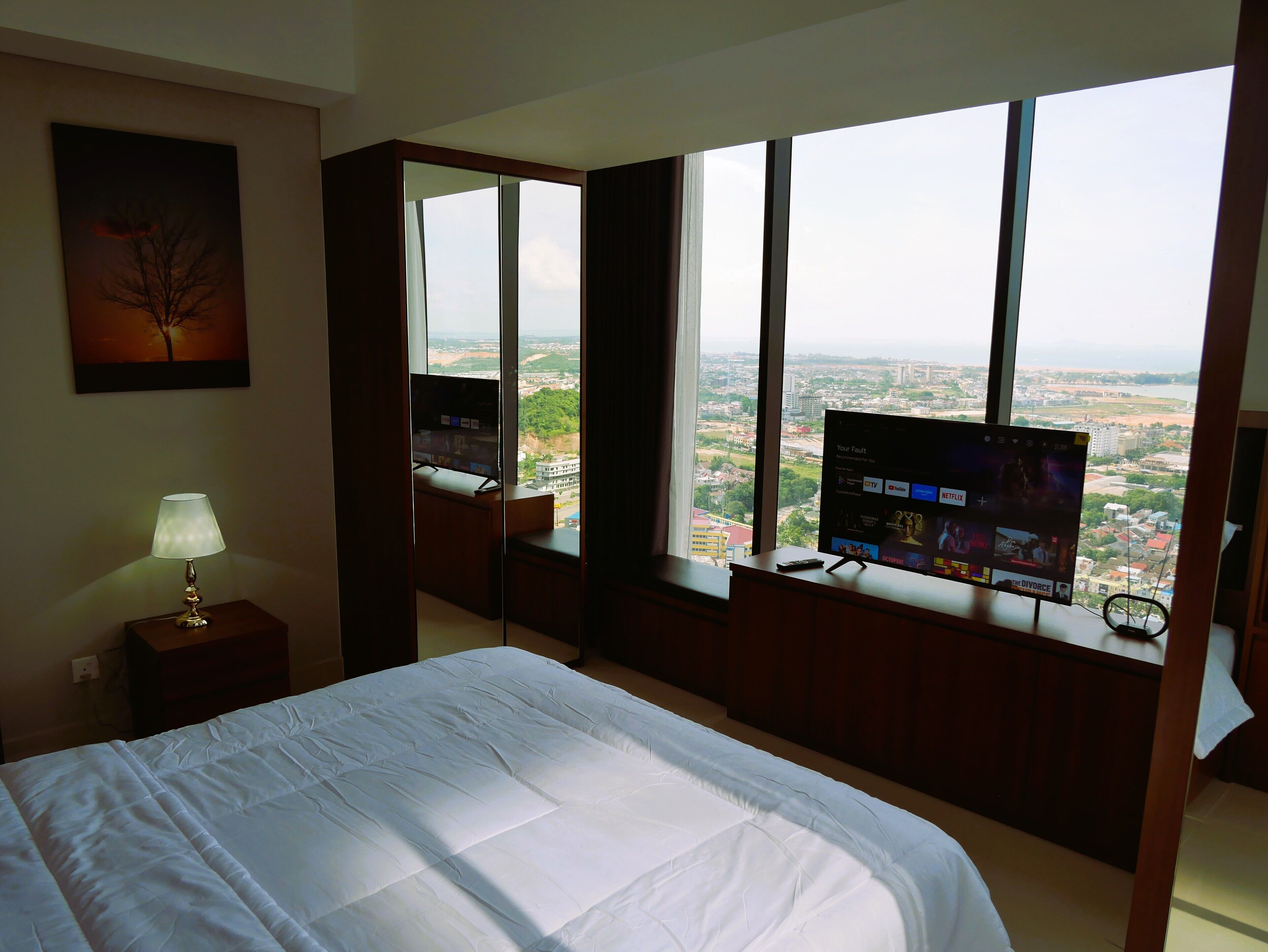 Una habitación de hotel con una cama grande, un televisor en el alféizar de la ventana, una lámpara y un cuadro en la pared.