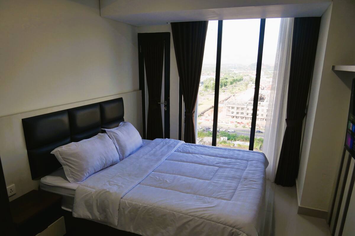 Une chambre à coucher avec un grand lit, une table de chevet et une fenêtre avec des rideaux.