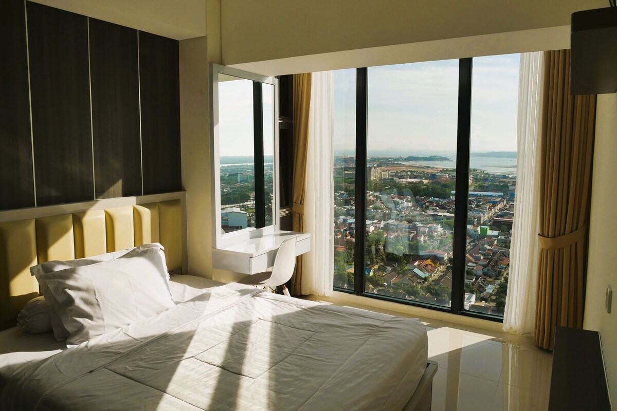 Une chambre d’hôtel avec un grand lit, un bureau et une vue sur la ville par la fenêtre.