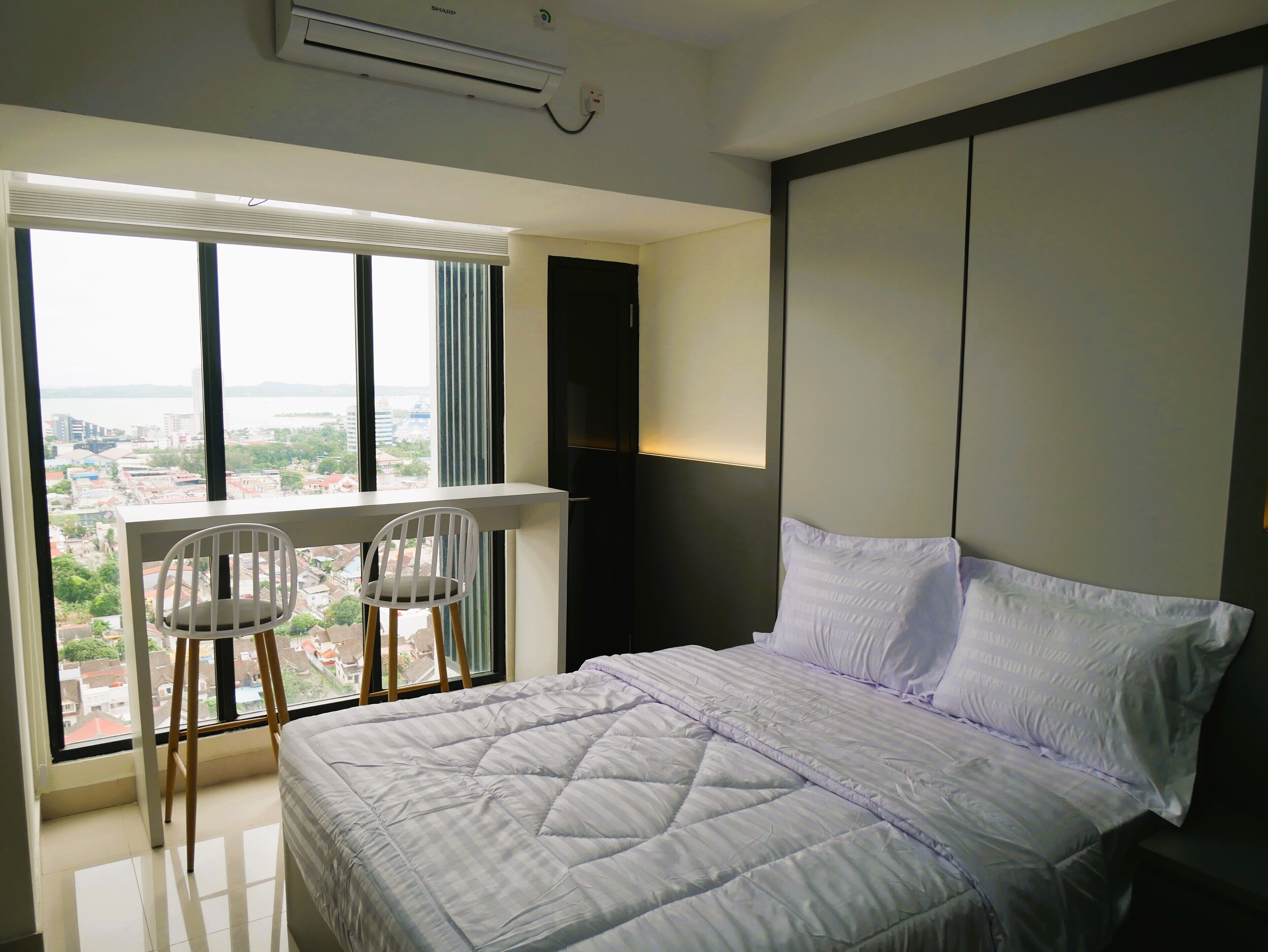 Un dormitorio con una cama grande, una silla, un televisor y vistas a un paisaje urbano a través de una ventana.