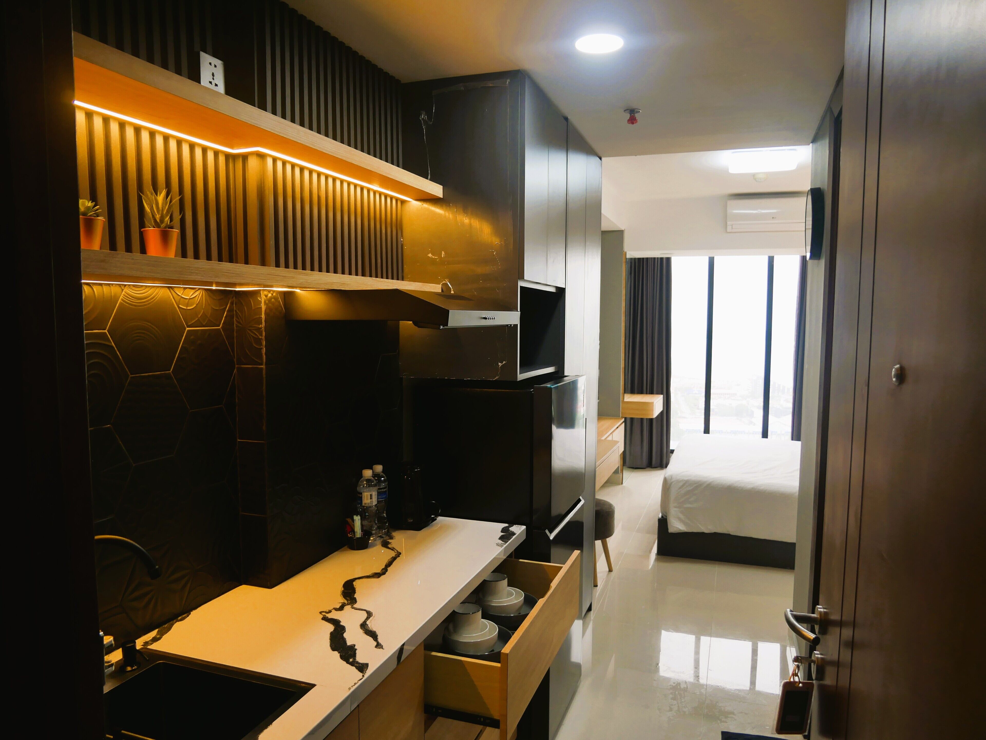A modern hotel room with a kitchen area, a bed, and a bathroom.