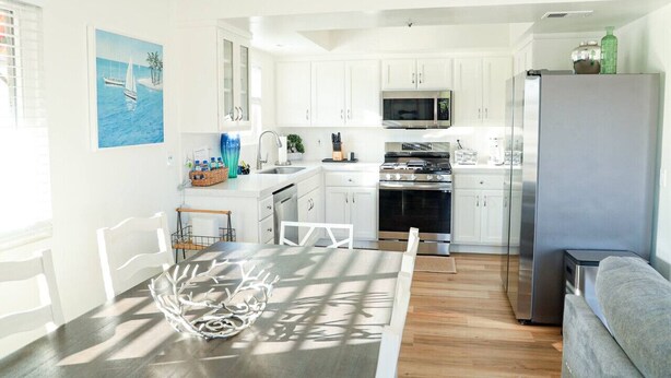 A modern kitchen with white cabinets, stainless steel appliances, and a dining area with a table and chairs. - Ocean View + Walk to Beach! Lovely SC Home (San Clemente)
