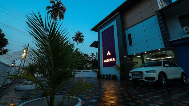 A modern building with a large sign reading "ALDORA" and a white car parked in front. - Aldora Airport Residency (Aluva)