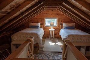 Cozy attic bedroom with two single beds, a nightstand, and a wooden bench.