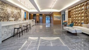 A modern lobby with a marble reception desk, bar stools, a sofa, and a bookshelf. - Shanxia Hotel (Bome)