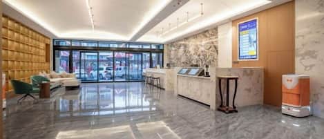 A modern hotel lobby with a reception desk, seating area, and large windows.