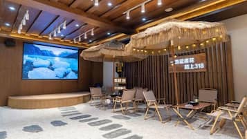 A room with a large screen, wooden panel walls, and seating arranged around a central table.