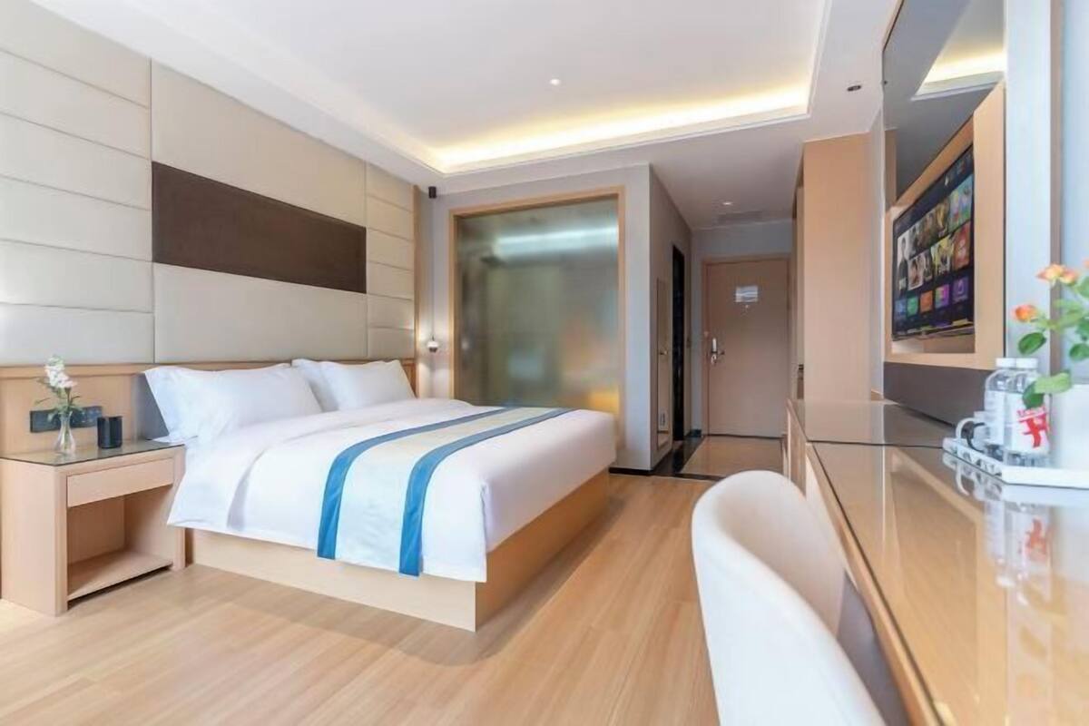 Quarto de hotel moderno com uma cama grande, mesa de cabeceira, escrivaninha e uma cadeira.
