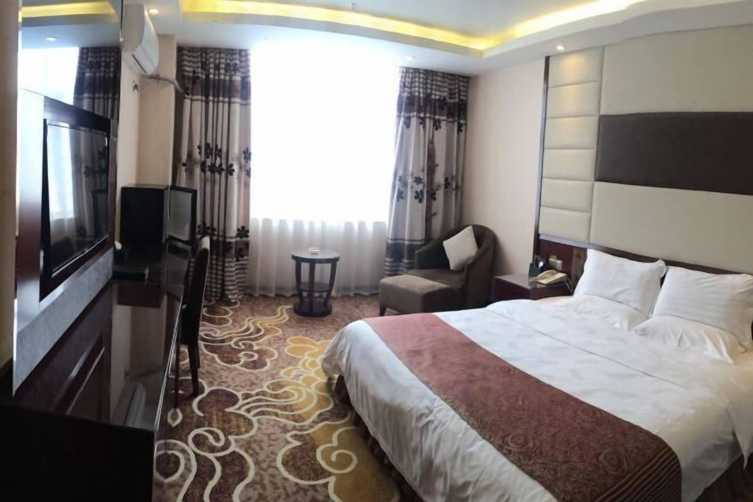 A hotel room with a large bed, a TV, a desk, and a chair.