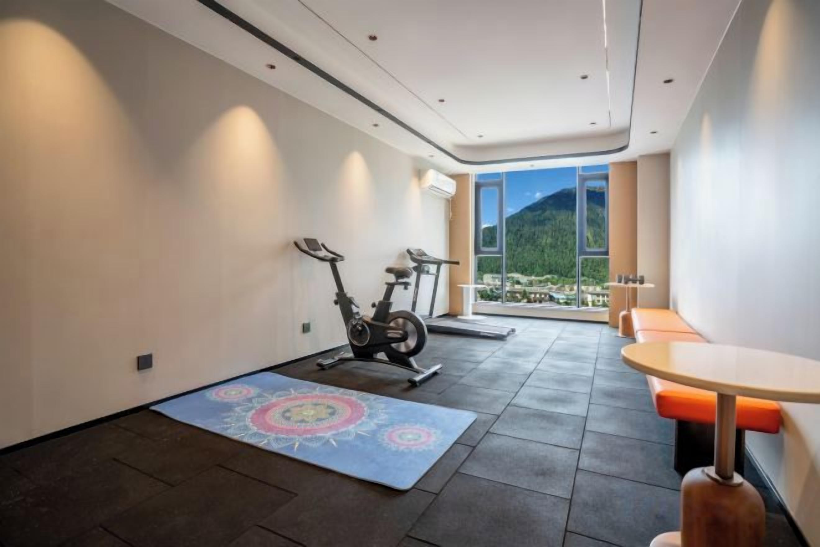 A modern room with a treadmill, a yoga mat, and a dining area with a view of mountains.