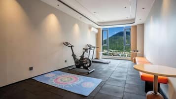 A modern room with a treadmill, a yoga mat, and a dining area with a view of mountains.