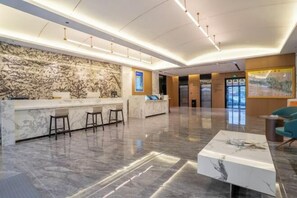 A modern lobby with a marble reception desk, bar stools, a coffee table, and a large wall mural. - Shanxia Hotel (Bome)