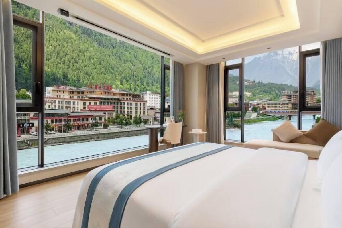 Quarto de hotel com uma cama grande, um sofá, uma mesa e vista para um rio e montanhas.