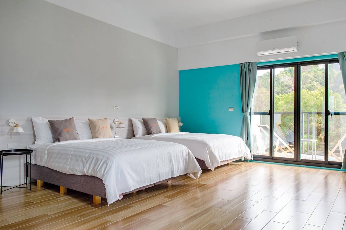 A modern bedroom with two beds, a large window with a view, and a wooden floor.
