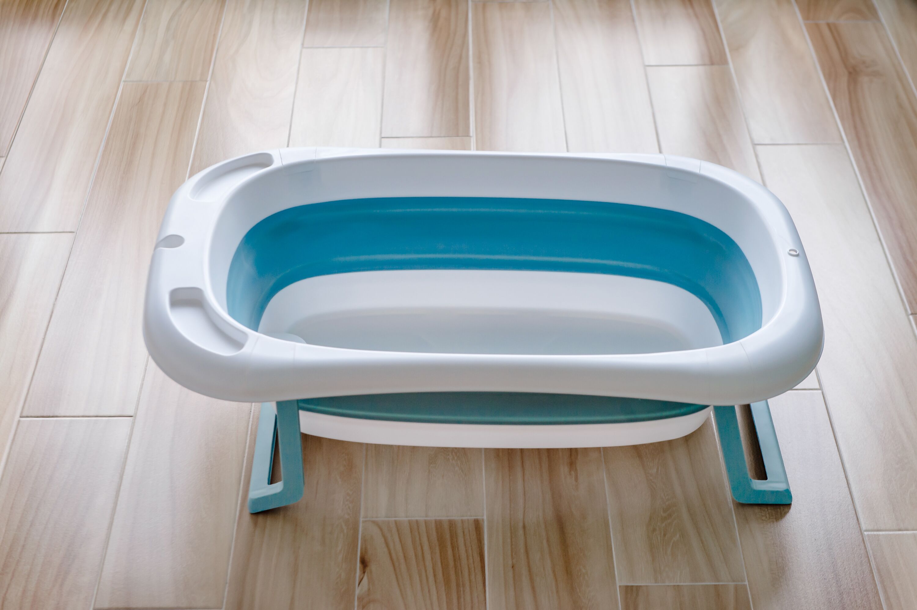 A portable bathtub with a white and teal design, placed on a wooden floor.