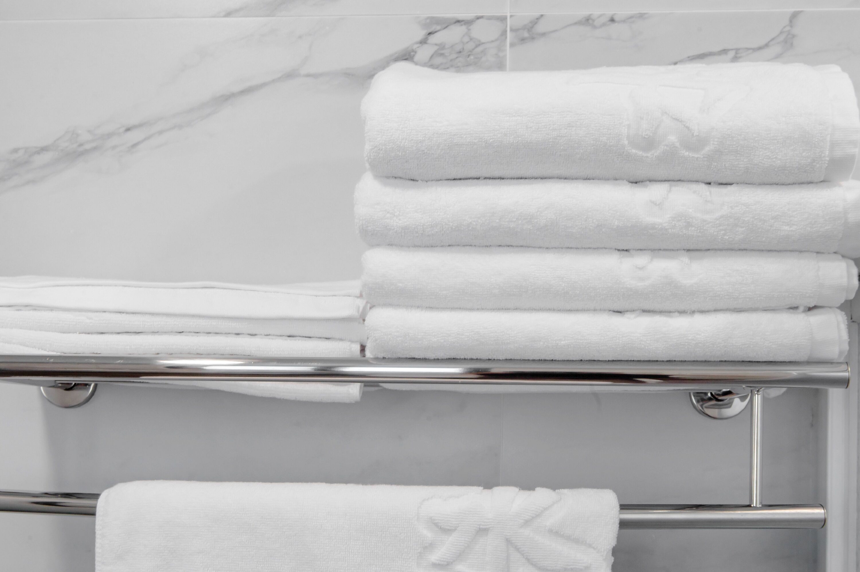A stack of white towels on a chrome towel rack in a bathroom with marble walls.