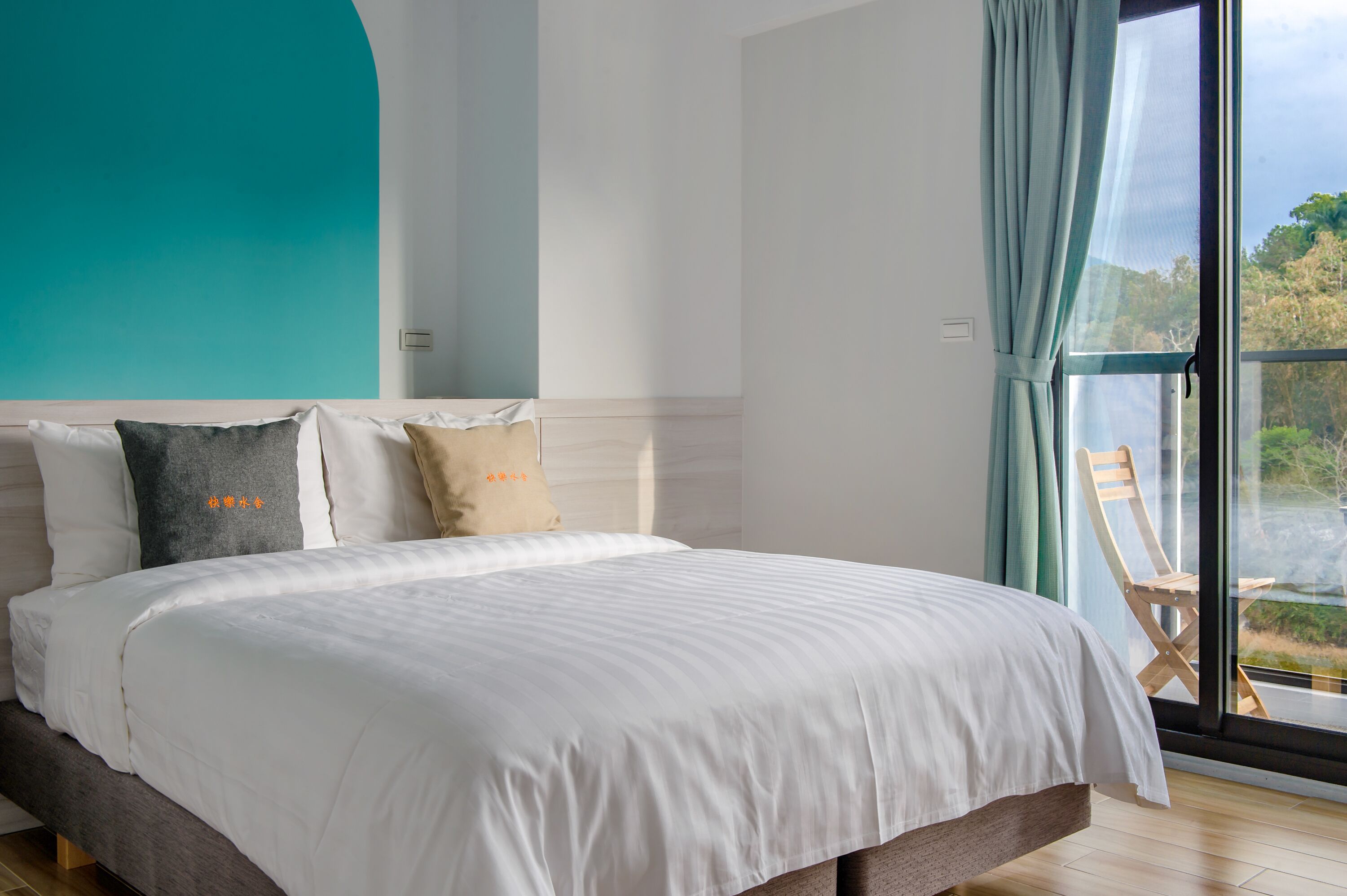 A bedroom with a large bed, a view of the outdoors through a window, and a teal accent wall.