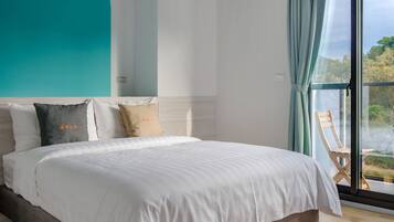 A bedroom with a large bed, a view of the outdoors through a window, and a teal accent wall.