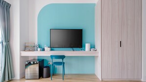 Una habitación moderna con una pared de acento color turquesa, un televisor de pantalla plana, un escritorio con silla, un armario y un cesto de basura.
