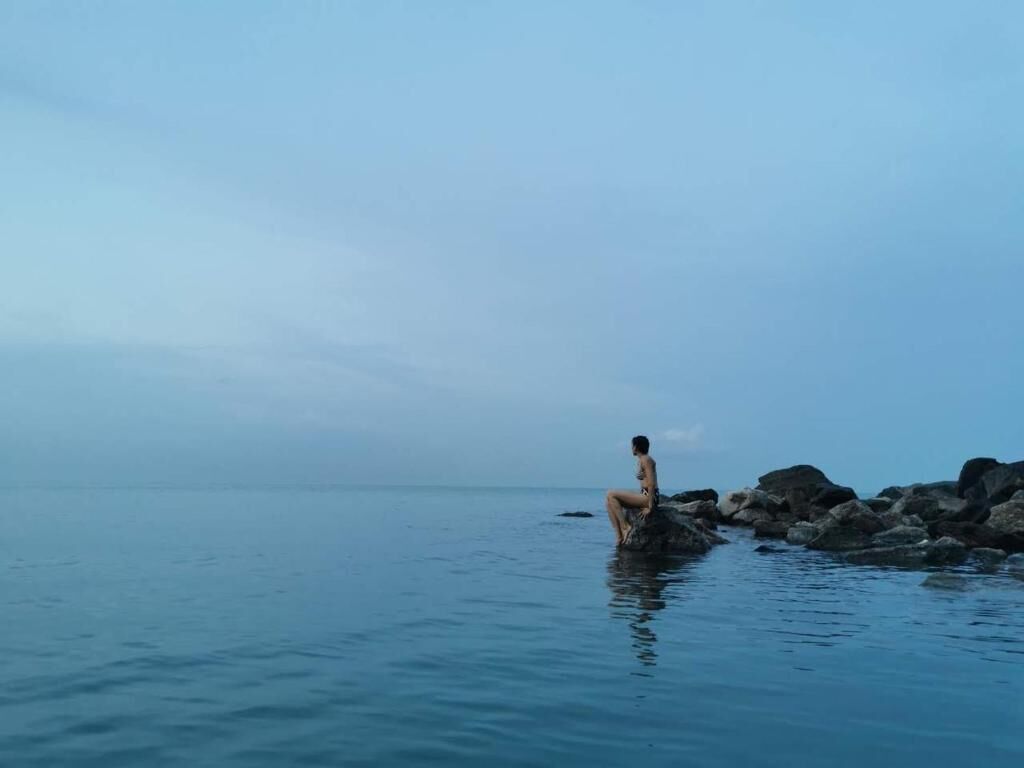 A person sitting on rocks by a calm body of water.
