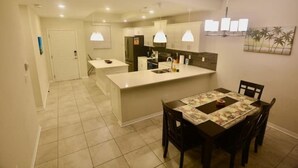 A modern kitchen with a central island, a dining area with a table and chairs, and a hallway leading to another room. - Storey Lake Water Park Resort Condo next to Disney (Kissimmee)