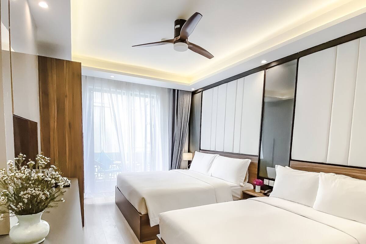 Una habitación de hotel moderna con dos camas, un ventilador de techo, un espejo grande y vistas al exterior.