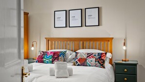 Een net opgemaakt bed met kleurrijke kussens, een houten hoofdbord en ingelijste certificaten aan de muur.