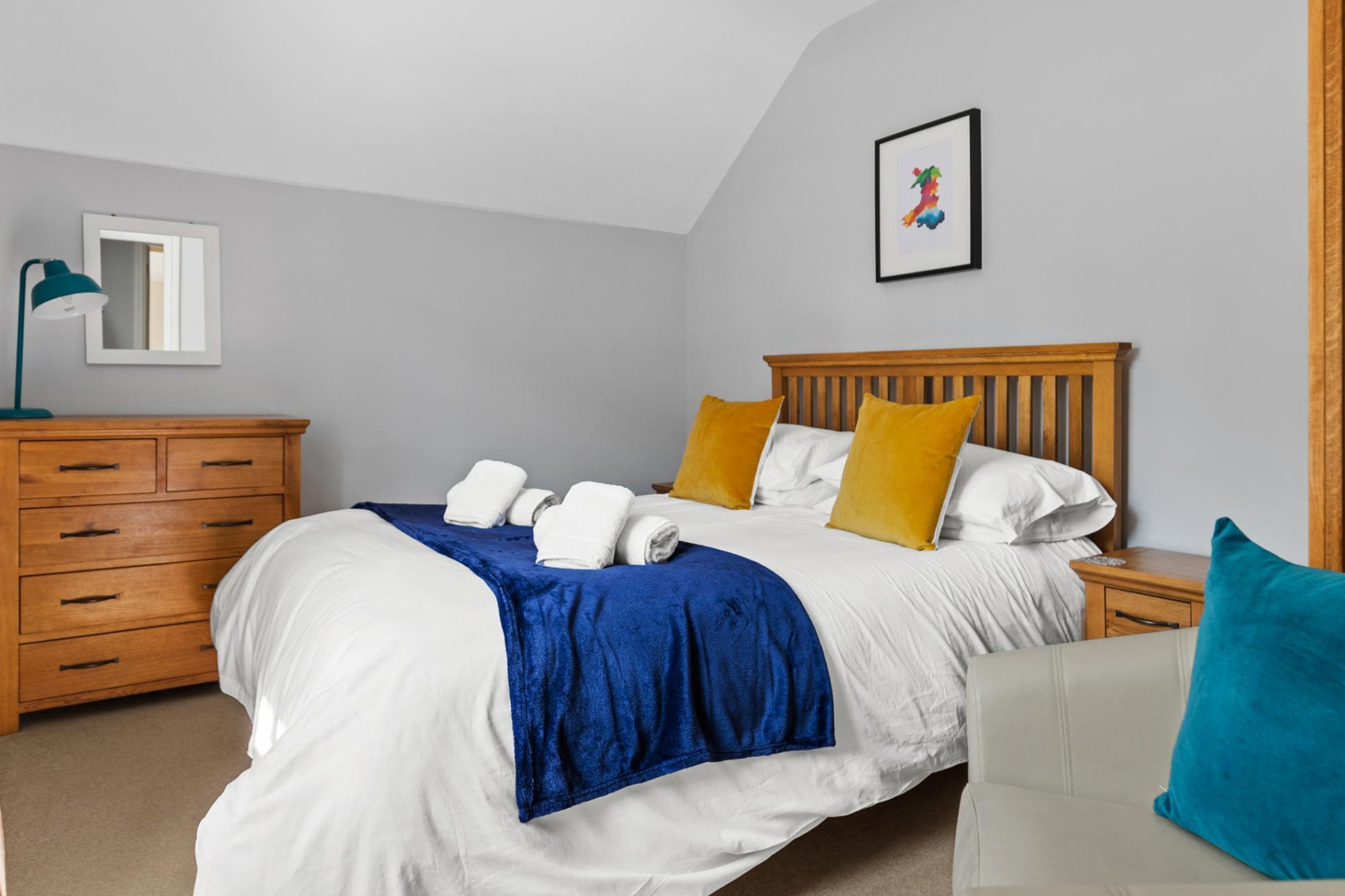 A bedroom with a bed, wooden nightstand, dresser, and a framed picture on the wall.
