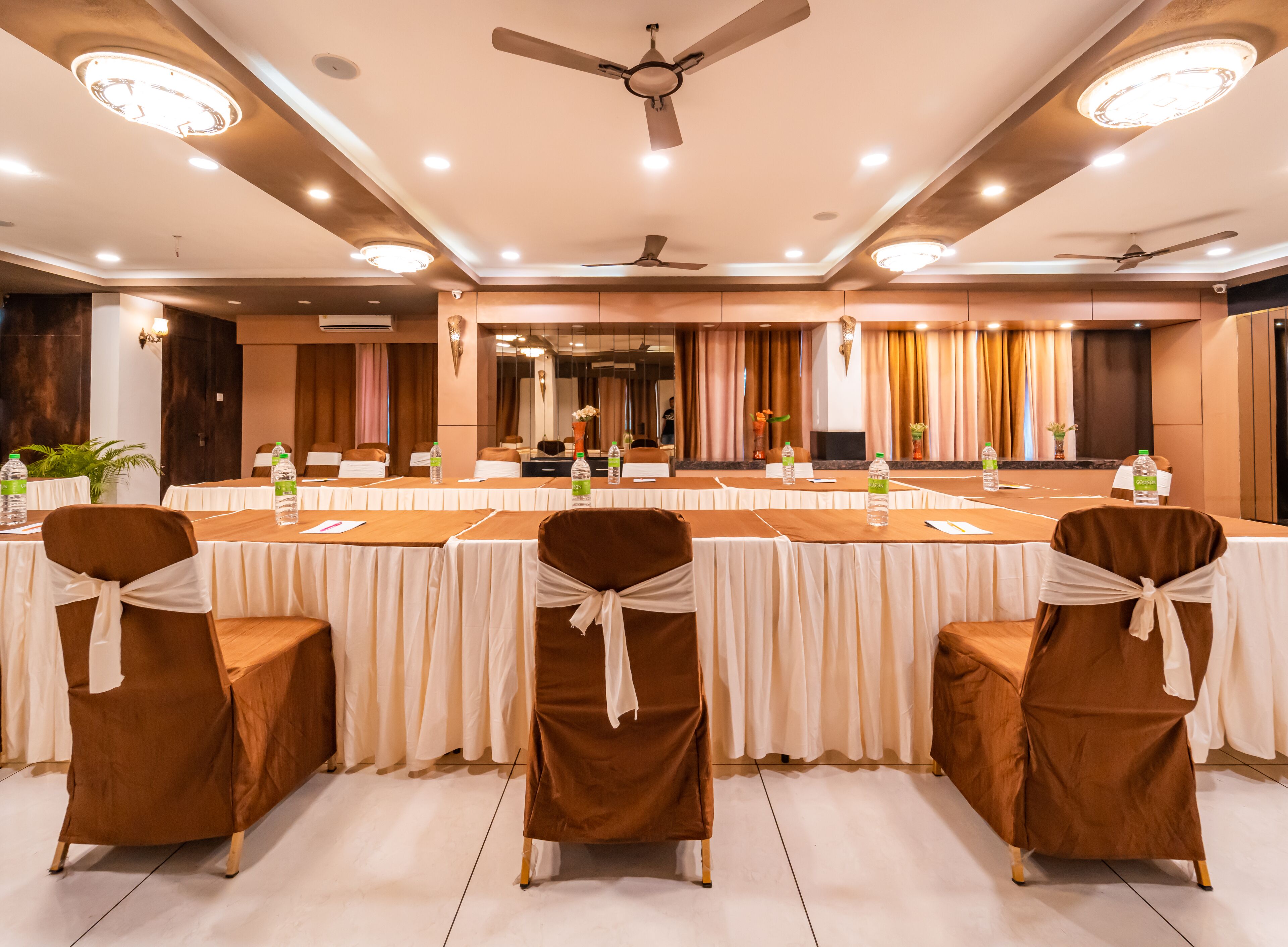 A conference room with a long table, brown chairs with white sashes, and ceiling fans.